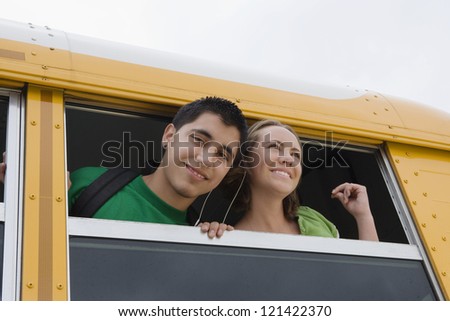 Low angle view of young male student listening music with classmate by a school bus window