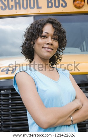 Portrait of a beautiful young woman standing with arms crossed against school bus