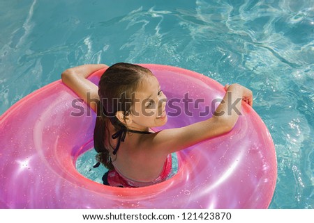 Happy Caucasian girl with inflatable tube in swimming pool