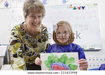 Portrait of female student showing her painting with teacher in art class