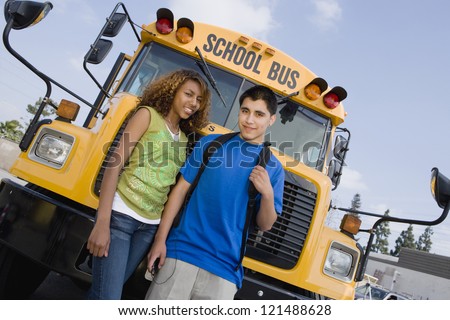Tilt shot of happy friends standing together in front of school bus