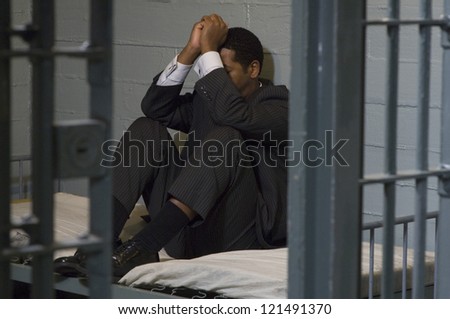 Full length of a depressed businessman sitting in jail - stock photo