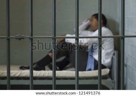 Side view of a unhappy business man sitting on bed in jail