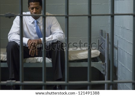 Depressed businessman sitting on bed behind a prison gate