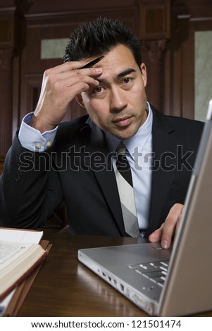 Portrait of a tense male advocate sitting with laptop in courtroom
