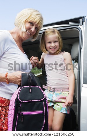 Portrait of mature woman helping granddaughter get down from minivan while holding her school bag