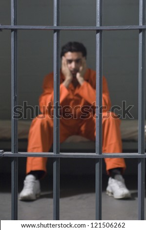Full length of a depressed criminal sitting behind bars