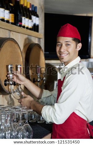Portrait of a young waiter standing by drinks tap