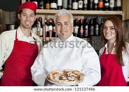 Portrait of a happy chef holding pizza with wait staff