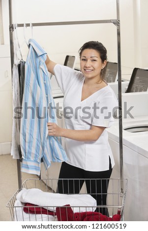 Happy young woman hanging shirt in front of washing machines in Laundromat
