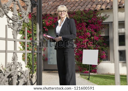 Happy senior real estate agent standing in front of house