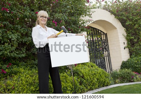 Happy senior female agent hammering sign board in lawn