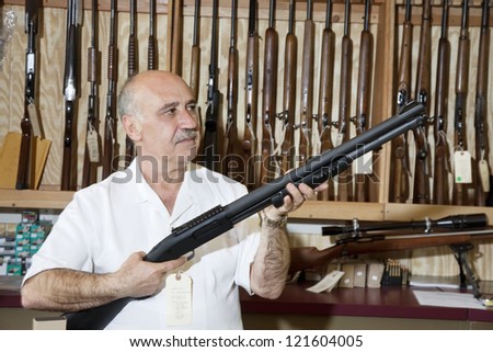 Middle-aged gun store owner looking at weapon in shop