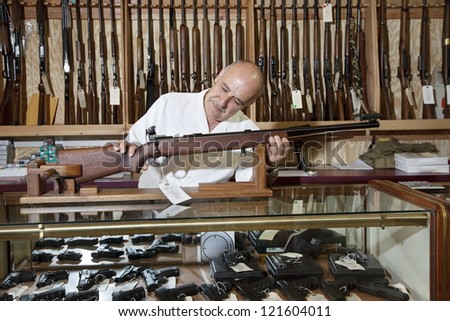 Middle-aged gun shop owner looking at rifle in store
