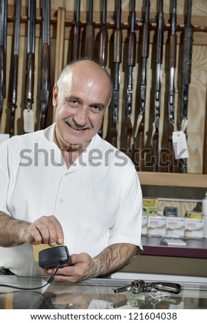 Portrait of a middle-aged merchant with credit card reader in gun shop