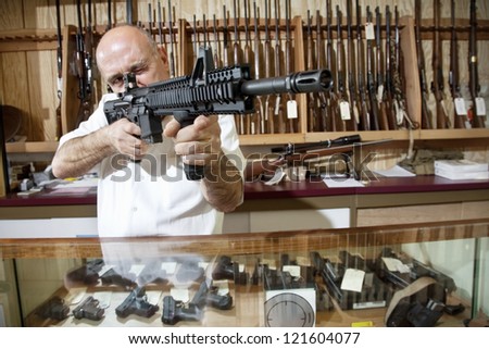 Middle-aged merchant aiming with rifle in gun shop