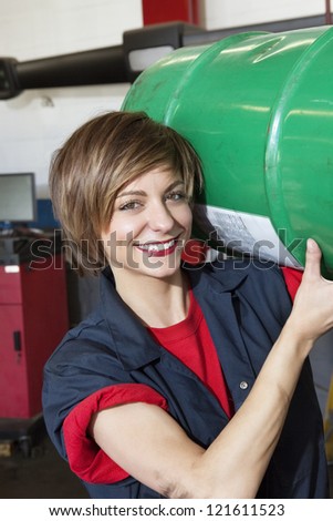 Portrait of a happy mechanic carrying oil drum in vehicle repair shop