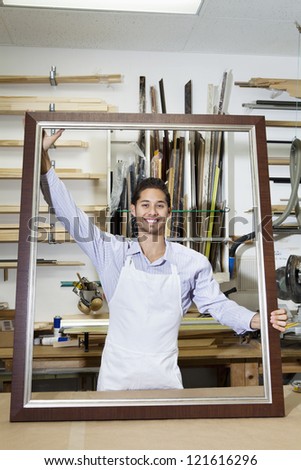 Portrait of a happy young craftsman holding big frame in workshop