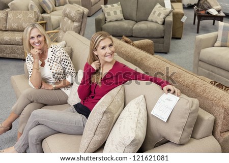 Happy Mother And Daughter Sitting On Sofa In Furniture Store