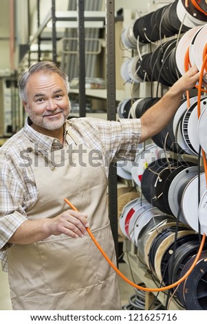 Portrait of a happy middle-aged store clerk with electrical wire spool in hardware shop