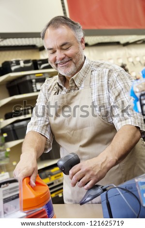 Happy middle-aged store clerk using bar code reader at checkout counter