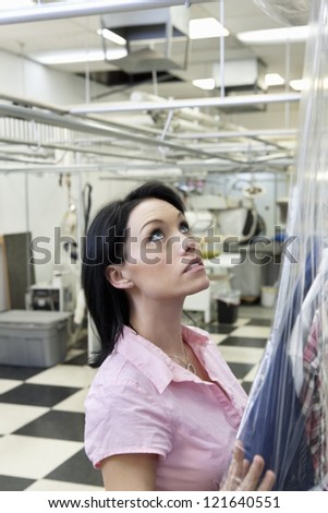 Beautiful young woman putting plastic to dry cleaned while looking up
