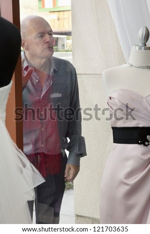 Senior man looking at wedding dress displayed on window in bridal store