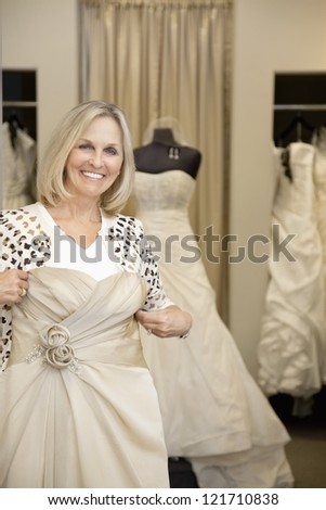 Portrait of a happy senior woman holding wedding gown in bridal store