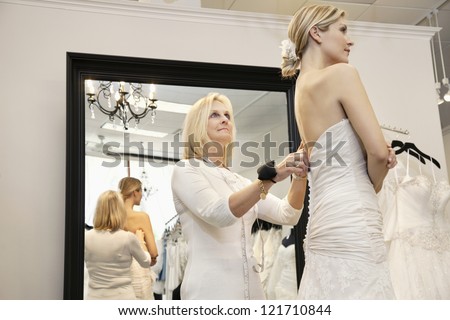Senior owner assisting young bride getting dressed in wedding gown