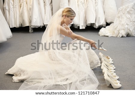 Side view of young woman in wedding dress confused while selecting footwear