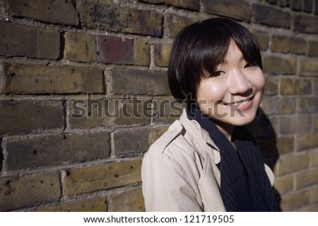 Portrait of a happy young Asian woman against wall