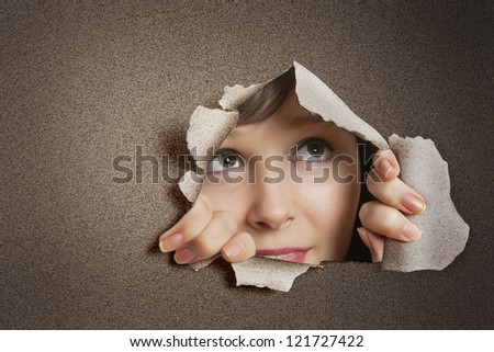 Young Caucasian woman peeking from ripped paper hole