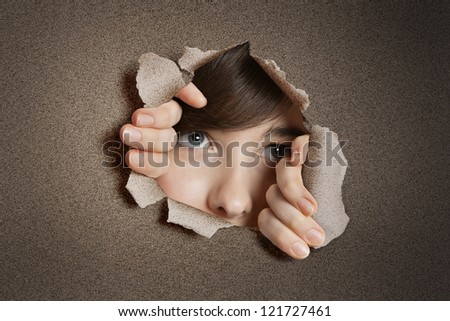 Young woman peeking from ripped white paper hole