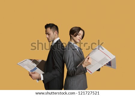 Business partners standing back to back while reading newspaper