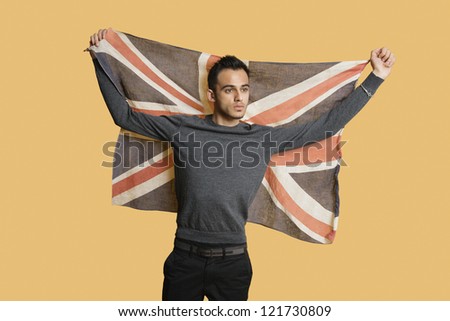 Young patriotic man lifting British flag over colored background