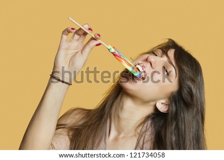 Portrait of a young woman eating lollipop over colored background