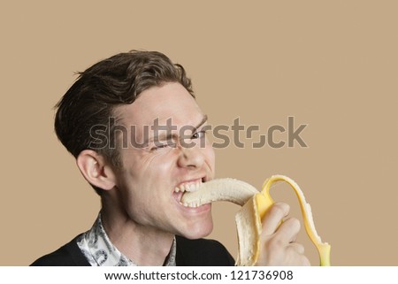 Portrait of a young man winking while biting banana over colored background