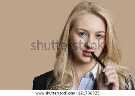 Portrait of a blond business woman with pen in mouth over colored background