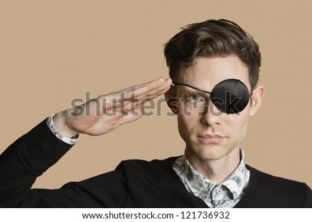 Portrait of a man wearing eye patch saluting over colored background
