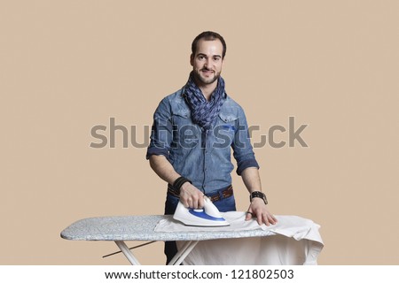 Happy young man ironing shirt over colored background