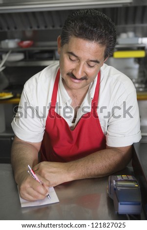 Hispanic waiter writing down order on a paper while standing at counter