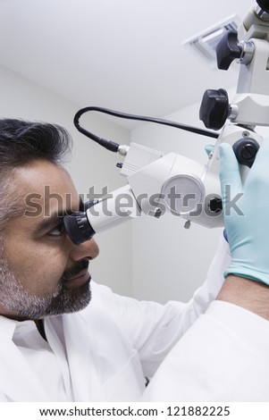 Indian male dentist operating microscope in clinic