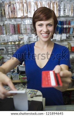 Portrait of young female sales clerk holding credit card at cash counter