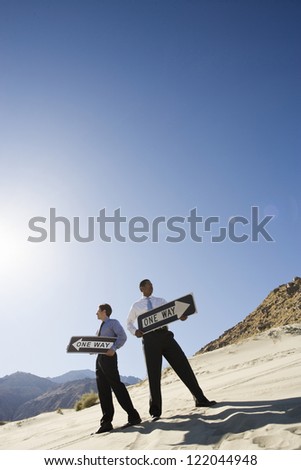 Low angle view of two businessmen standing with sign board in opposite direction at desert