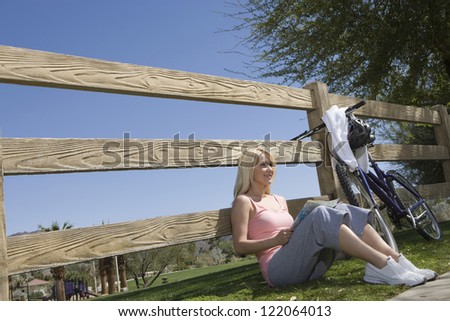 Beautiful happy young female sitting by fence with road map besides a bicycle