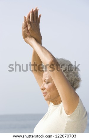 Side view of an African American senior woman practicing yoga against sky