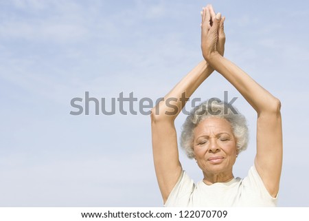 An African American senior woman practicing yoga against sky