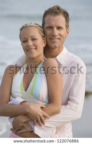 Portrait of middle aged man embracing woman from behind at beach