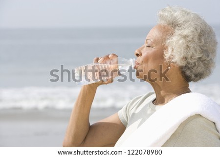An African American senior woman drinking water from bottle with sea in the background