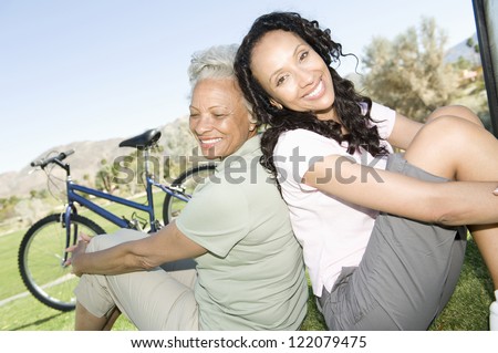Happy African American mother and daughter enjoying while sitting on grass in park